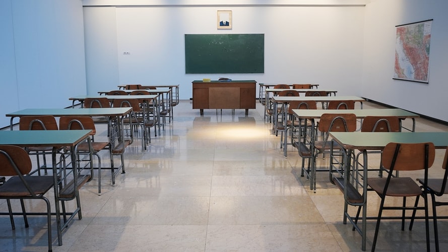 Sala de aula com mesas e cadeiras de madeira e um quadro negro.